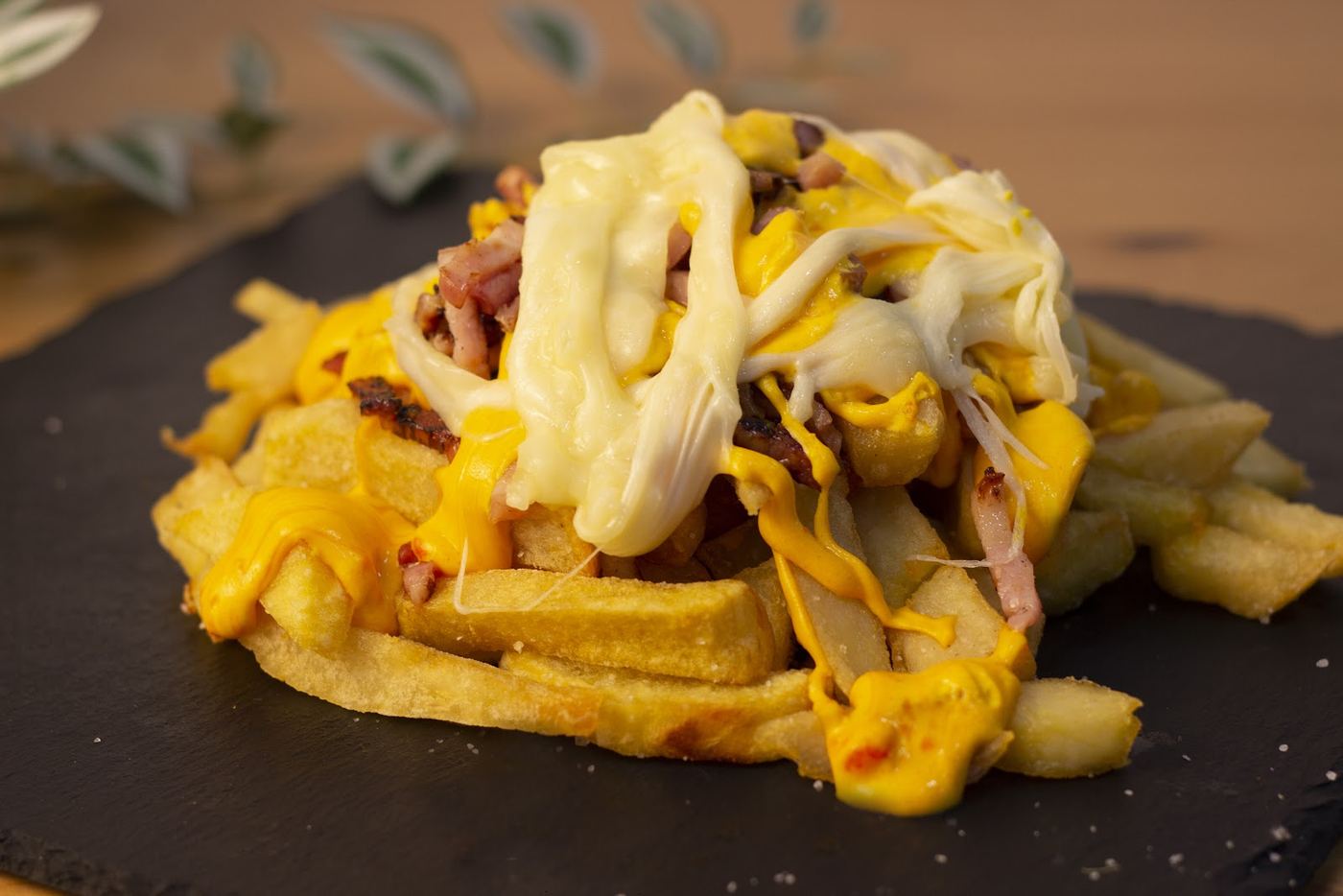 Patatas fritas caseras con queso fundido y bacon crujiente.